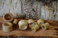 Load image into Gallery viewer, Several Holz Flesh Tunnel Krokodilholz hell leicht konvex double flared plugs in different sizes are scattered on rough wood, with a textured tree bark background.
