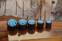 Cargar imagen en el visor de la galería, Five Tunnel Sonoholz Resin Türkis Inlay Spiralbögen, each with carved rose designs, are arranged by size beside a transparent ruler on a wooden surface, with a textured bark backdrop.
