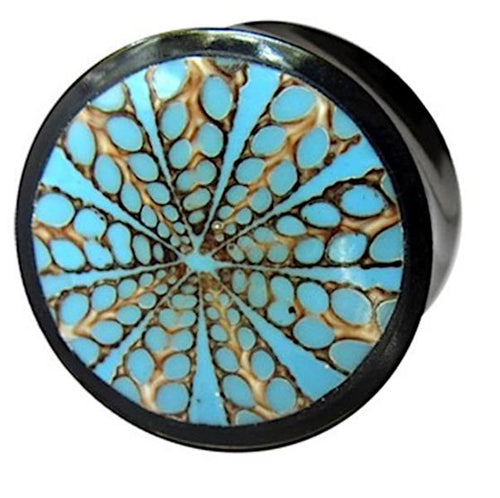 The Horn Plug Spinnennetz blau is a round black plug hand-carved from Büffelhorn, featuring a blue and brown geometric starburst pattern on its face.