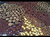 Load image into Gallery viewer, A close-up of assorted chocolates and candies in brown and gold wrappers, arranged in intricate circular and hexagonal patterns—mirroring the design of the Plug braun Holz Baum des Lebens dunkel Gravur Flechtrand.
