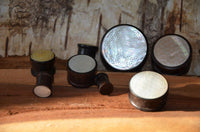 Load image into Gallery viewer, A set of round "Holz Plug Perlmutt Inlay Gravur Blume des Lebens ribbed" with geometric flower-of-life designs is displayed on a wooden surface against a rustic bark background.
