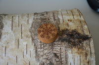 Load image into Gallery viewer, A small, round Holz Teakholz Plug Awe Helm braun double flared, featuring an intricate snowflake design inspired by nordische Mythologie Schmuck, rests on birch bark with a striking mix of dark and light patches.
