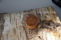 Load image into Gallery viewer, A Holz Teakholz Plug Sonnen Maske double flared, featuring an intricate carved design, rests on the textured surface of a birch tree log.
