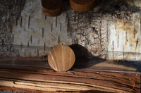 Load image into Gallery viewer, The Holz Teakholz Plug Sonnen Maske double flared lies on a clear ruler atop textured wood with bark, while sunlight casts shadows that highlight the plug's natural teak grain and the rustic background.
