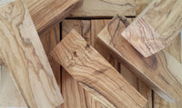 Load image into Gallery viewer, Several rectangular blocks of light-colored wood with wavy grain patterns are stacked and scattered, highlighting the natural textures found in Olivenholz Flesh Tunnel double flared abgerundet Holz.
