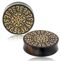 Load image into Gallery viewer, Two round, dark Holz Flesh Plug Tamarinde Holz Krokodilholz Kreuz Ranken with intricate, light floral and swirl mandala carvings are displayed on a white background with a subtle reflection.
