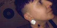 Load image into Gallery viewer, Close-up of a person with short purple hair and shaved sides wearing a large round Holz Plug Perlmutt Inlay Gravur Blume des Lebens ribbed earring and a nose ring. Musical notes and a vinyl record are on the wall behind them.
