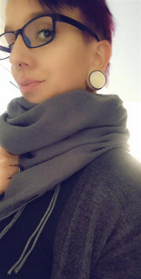 Load image into Gallery viewer, Person with glasses, a nose ring, and large circular Holz Plug Perlmutt Inlay Gravur Blume des Lebens ribbed earrings, wearing a thick gray scarf and dark top, looks at the camera in soft lighting.
