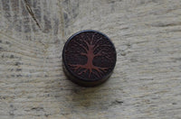 Load image into Gallery viewer, A round, dark token engraved with a tree design—symbolizing growth and connection—inspired by the Flesh Plug Holz Sonoholz Baum des Lebens double flared, rests on a textured wooden surface.
