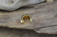 Load image into Gallery viewer, A small, crescent-shaped Saddle Plug Messing antik gold Sichel Bögen Tunnel with ornate engravings rests on a weathered wooden surface.
