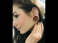 Load image into Gallery viewer, A person with long brown hair and a nose piercing wears the Krokodil Holz Plug Baum des Lebens hell double flared featuring a tree design, holding their hand near their ear and looking to the side.
