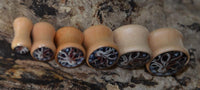 Load image into Gallery viewer, Six Holz Plug Oktopus Krake Bild beige hell double flared ear plugs of various sizes, each featuring an intricate swirled design on one end, are lined up on a textured, bark-like surface.
