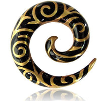 Load image into Gallery viewer, The Brass Piercing Dehnschnecke features a black resin spiral with elegant gold swirls, ideal for lobe piercings. Its unique shape resembles a stylized G or curled horn, displayed on a white background with a subtle reflection.
