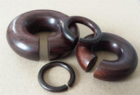 Load image into Gallery viewer, Two Piercing Narraholz Holz Expander dunkelbraun groß Ohrstecker rings are displayed in two interlocking parts on a beige surface, highlighting their unique puzzle-like design for ear stretching.
