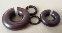 Load image into Gallery viewer, Four polished Piercing Narraholz Holz Expander rings in dark brown, each with a single cut and varying sizes, rest on a light brown surface—a stylish choice for lobe piercing fans seeking groß Ohrstecker Ring Bogen Dehner.
