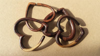 Load image into Gallery viewer, Five handcrafted wooden bangles with organic shapes overlap on a plain brown surface. The dark brown wood, similar to Piercing Narraholz Holz Expander dunkelbraun Herz Dehner, displays varied tones and highlights its natural grain.
