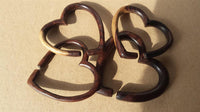 Load image into Gallery viewer, Three interlocking wooden hearts, each carved from dark brown Narraholz like the Piercing Narraholz Holz Expander dunkelbraun Herz Dehner, arranged on plain cardboard with sunlight casting soft shadows.

