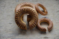 Load image into Gallery viewer, A set of carved wooden rings, featuring the Ohr Donut Piercing griechisch Jackfrucht Holz with geometric patterns and open gaps, arranged on a textured wooden surface.
