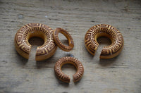 Load image into Gallery viewer, Four circular Ohr Donut Piercing griechisch Jackfrucht Holz expanders, each with a notch and intricate Greek meander designs, are arranged on a wooden surface.
