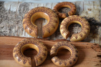Load image into Gallery viewer, Five circular Ohr Donut Piercing pieces, crafted from Jackfrucht Holz and inspired by a Pfau Mandala, feature brown patterns and slits. Displayed on rough bark, their polished wood highlights the intricate mandala designs.
