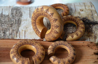 Load image into Gallery viewer, Ohr Donut Piercing Pfau Mandala Jackfrucht Holz napkin rings, featuring intricate dark mandala patterns and an open slit for easy use, are displayed on a rustic wooden surface and birch bark.
