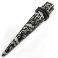 Load image into Gallery viewer, The Totenkopf Piercing Expander Dehnungsstab is a black straight ear stretcher with a white skull and crossbones design and a removable rubber o-ring near the wider end.
