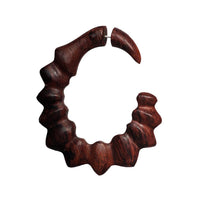 Load image into Gallery viewer, A single large, hand-carved fake piercing made of light and dark brown sonoholz and stainless steel, featuring a unique wavy jagged circular design, is displayed against a plain white background.
