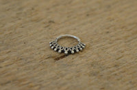 Load image into Gallery viewer, A Piercing Ring 925 Silber Labret Tragus Septum Mandel featuring ornate loops and dots rests on a textured wooden surface.
