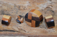 Load image into Gallery viewer, Four "laminiert Holzplug vier Farben Muster Tribal Holz Plug" in various shapes and wood patterns are arranged on a textured wooden surface, with the largest piece being round and others smaller, featuring dark and light wood designs.

