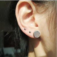 Load image into Gallery viewer, A close-up of an ear with two silver studs and a Fake Plug Piercing Edelstahl 10mm Blume des Lebens Viking in the lobe, all illuminated by sunlight.
