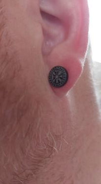 Load image into Gallery viewer, A close-up of a person's ear wearing the Edelstahl Ohrstecker schwarz 8-10mm Viking Celtic Nordic, showing its black circular design with a compass motif and subtle facial hair for a distinct Viking-inspired look.
